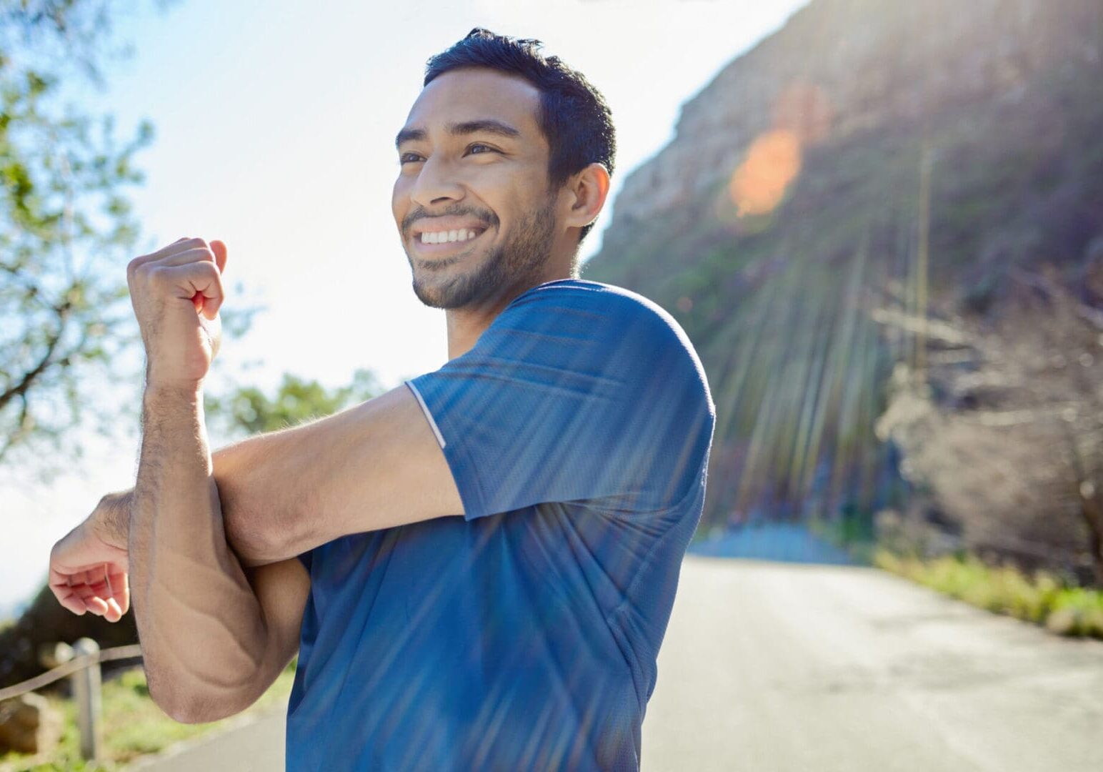 Smiling man stretching outdoors on sunny day.