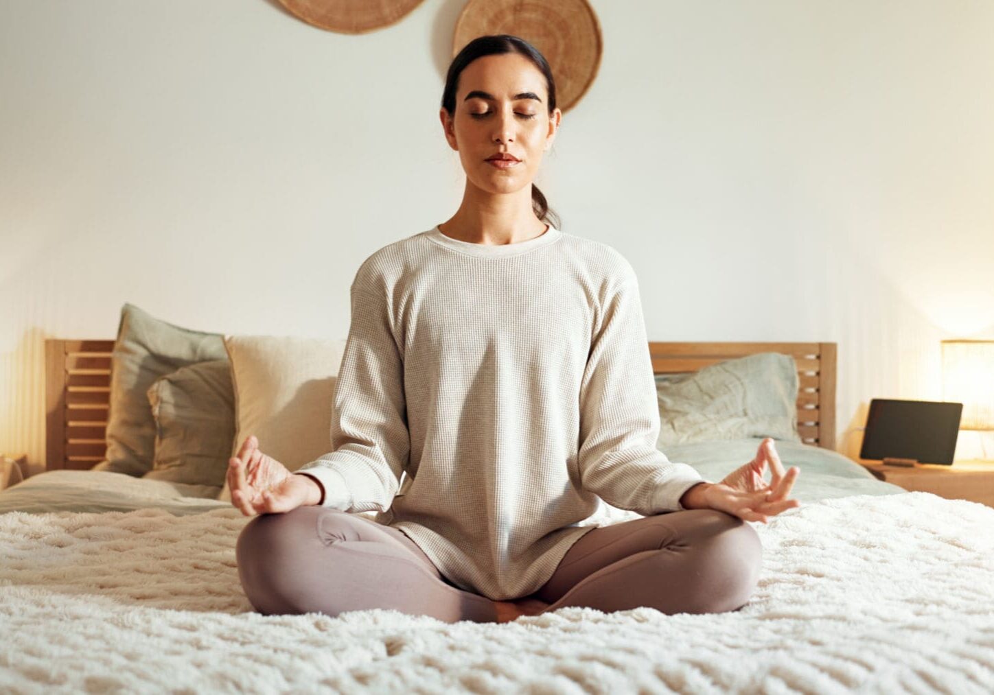 Woman meditating on bed in cozy room.