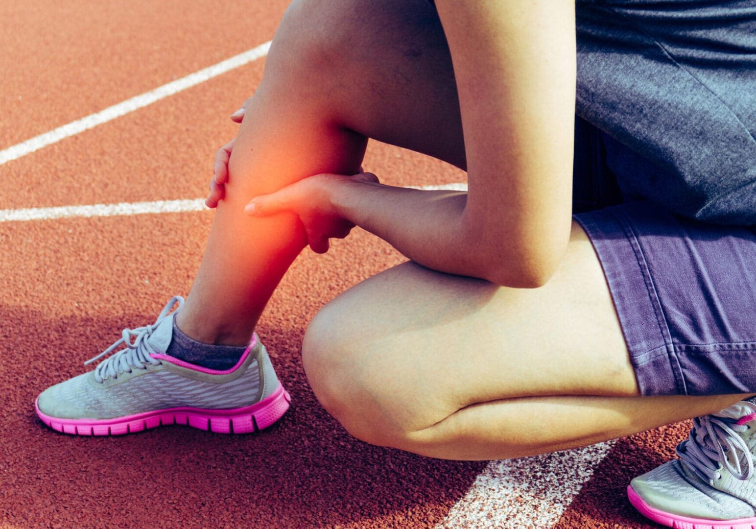 Person holding injured leg on running track.