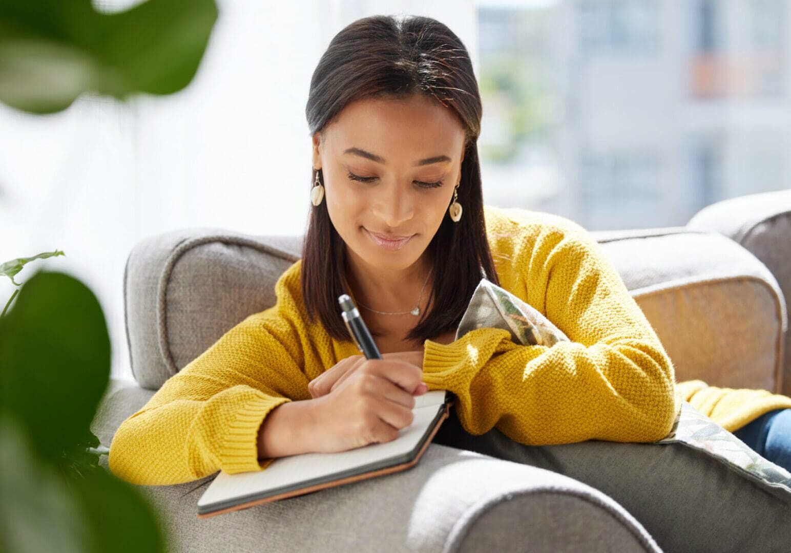 Woman writing in notebook on couch.